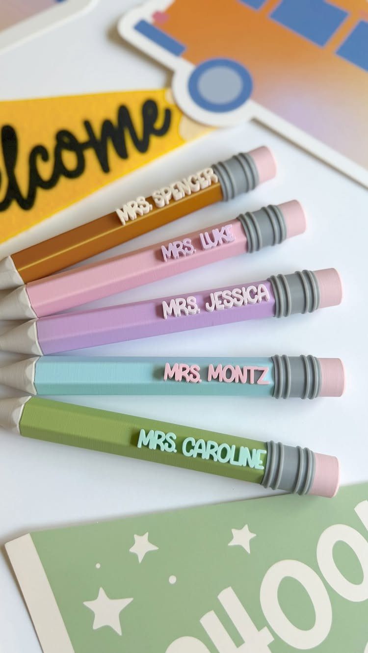 Colorful personalized pencil pens with teacher names arranged on a white surface.
