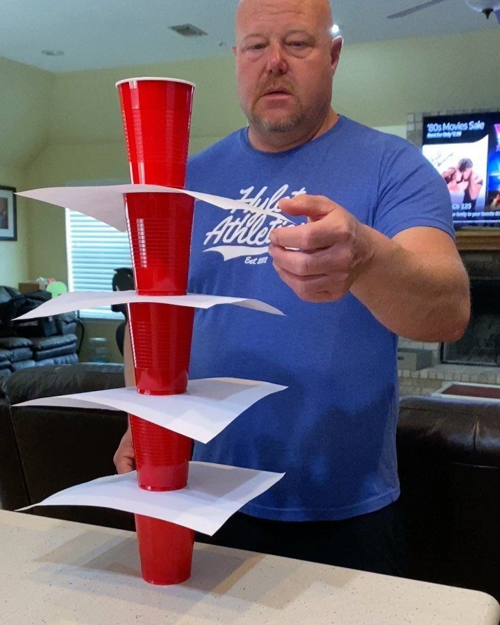 Man playing a game with a tower of red cups and white paper.
