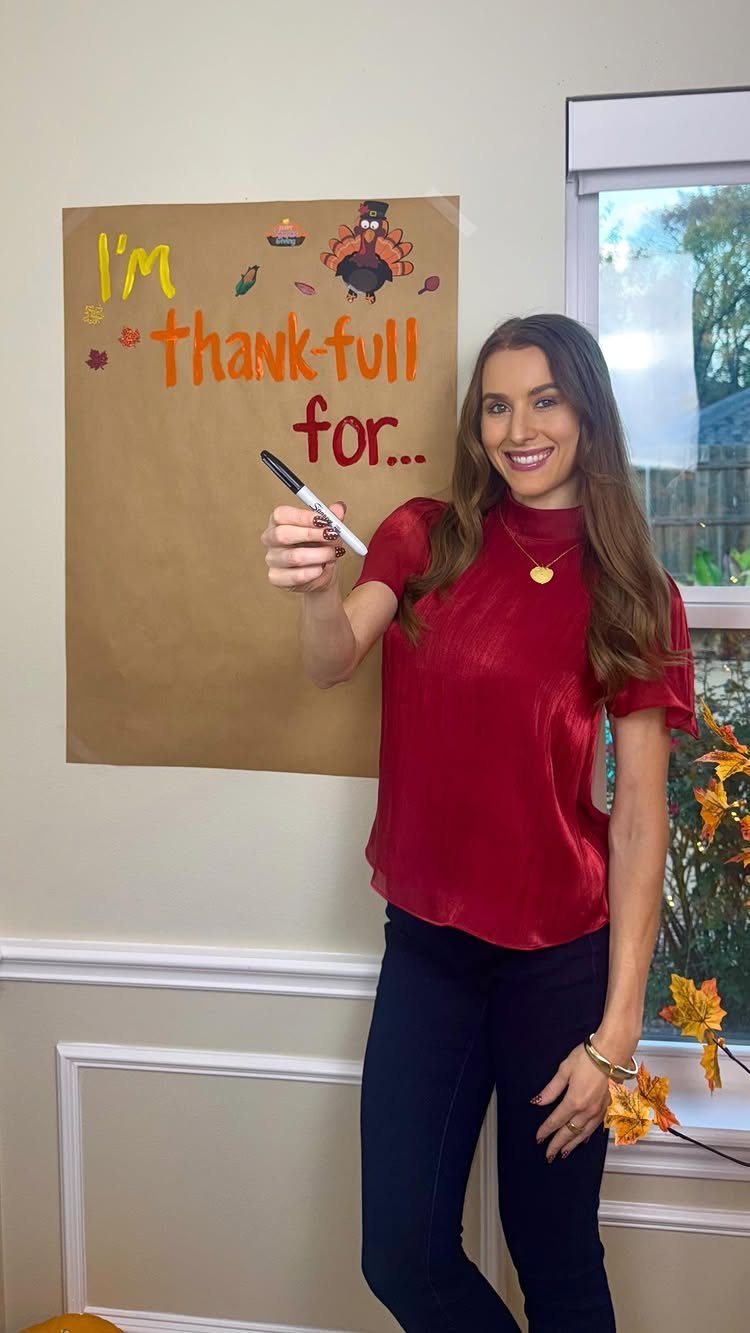Woman holding a marker next to a Thanksgiving gratitude poster in a room.