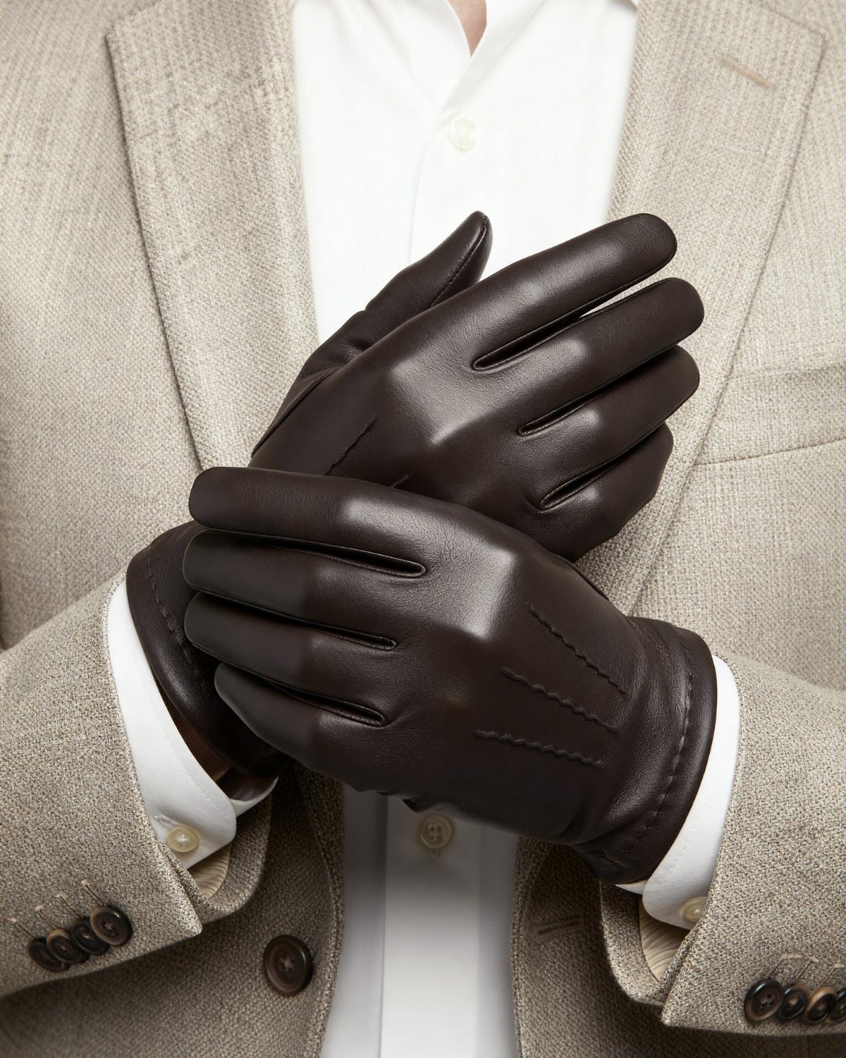 Dark brown leather gloves worn by a man in a grey blazer.