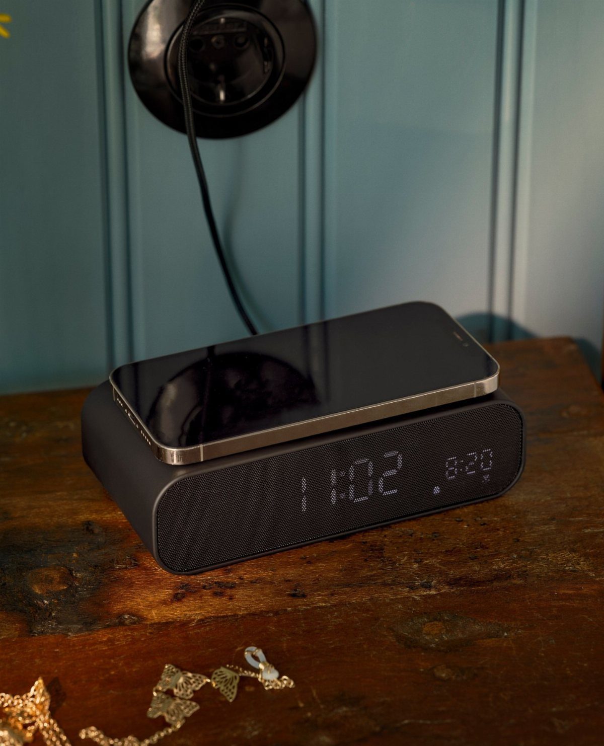 Black digital alarm clock speaker with a smartphone resting on top on wooden table