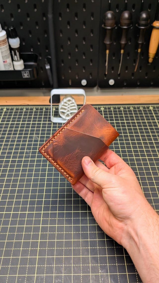 Handmade brown leather wallet held over a green cutting mat in a workshop