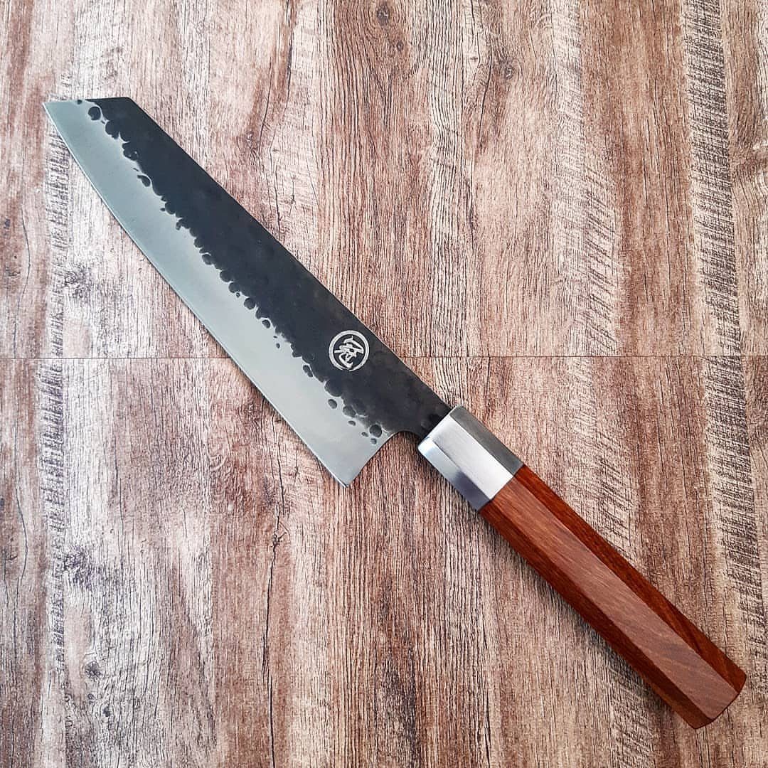 Japanese chef's knife with hammered steel blade and wooden handle on wood background