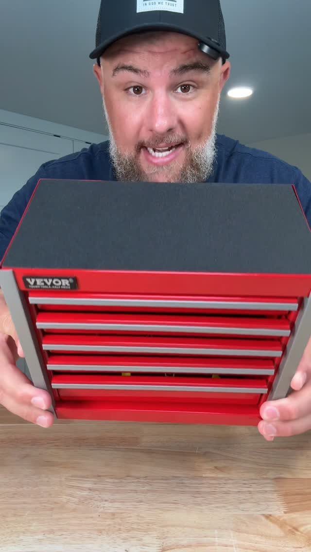 Man holding a small red metal tool chest with multiple drawers on wooden table