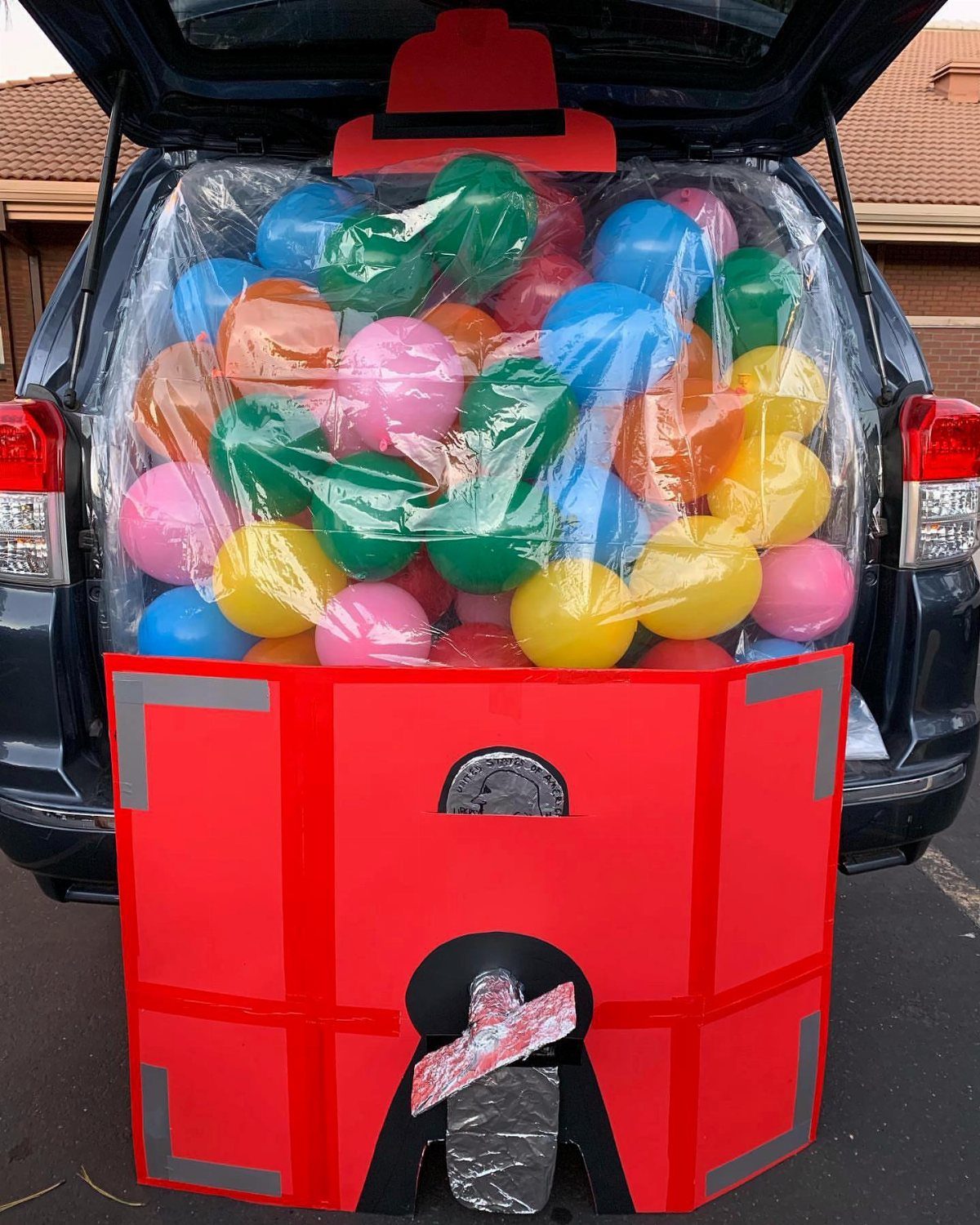Car trunk decorated as a red arcade claw machine filled with colorful balloons.