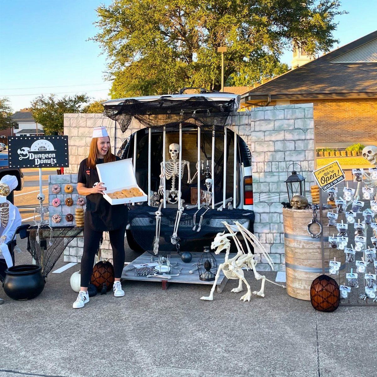 Woman holding donuts in front of a car trunk decorated as a spooky dungeon.