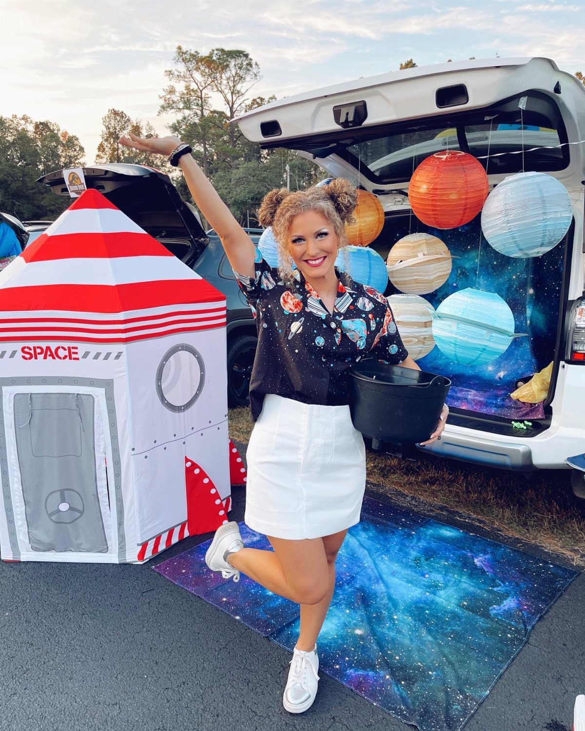 Woman posing with a space-themed car trunk featuring planet lanterns and a rocket ship.