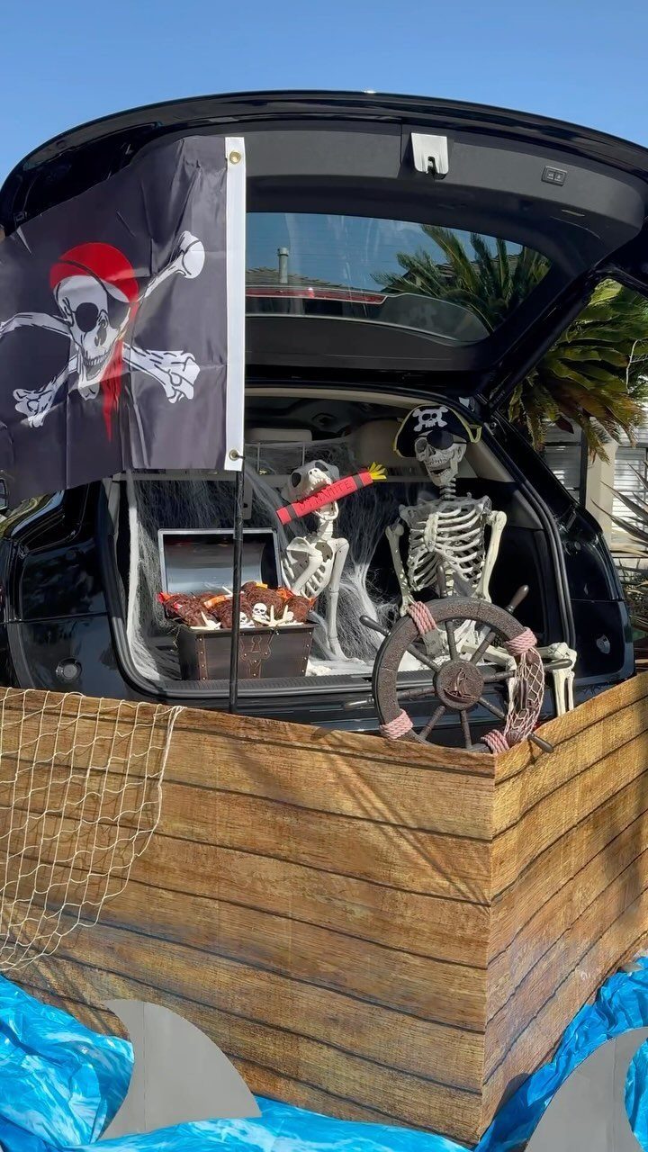 Pirate ship trunk-or-treat display with skeletons, a ship wheel, and a pirate flag.