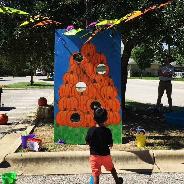 Child playing a pumpkin-themed bean bag toss game at a trunk or treat event.