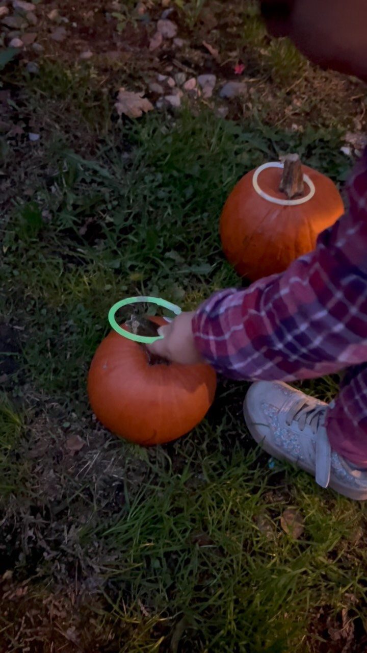 Child tossing a green ring onto an orange pumpkin during a ring toss game.
