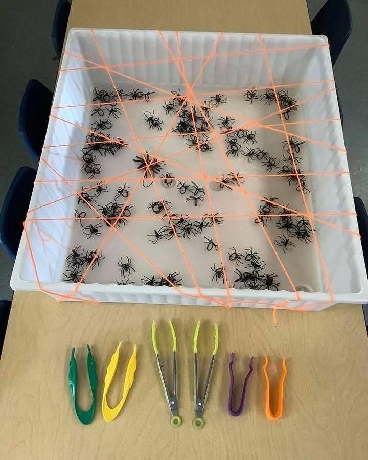 Plastic spiders in a bin with orange string and colorful tongs for games.