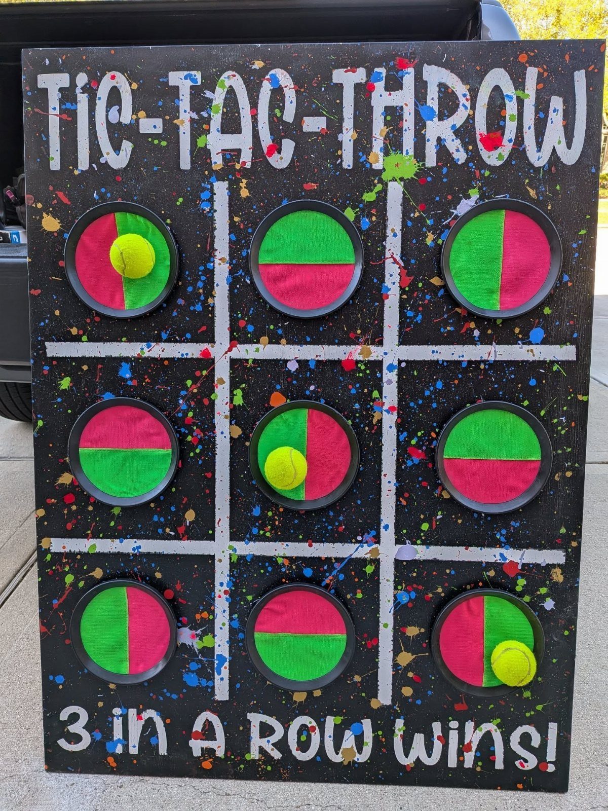 Tic-Tac-Throw game board with colorful splatters and yellow balls for trunk or treat.