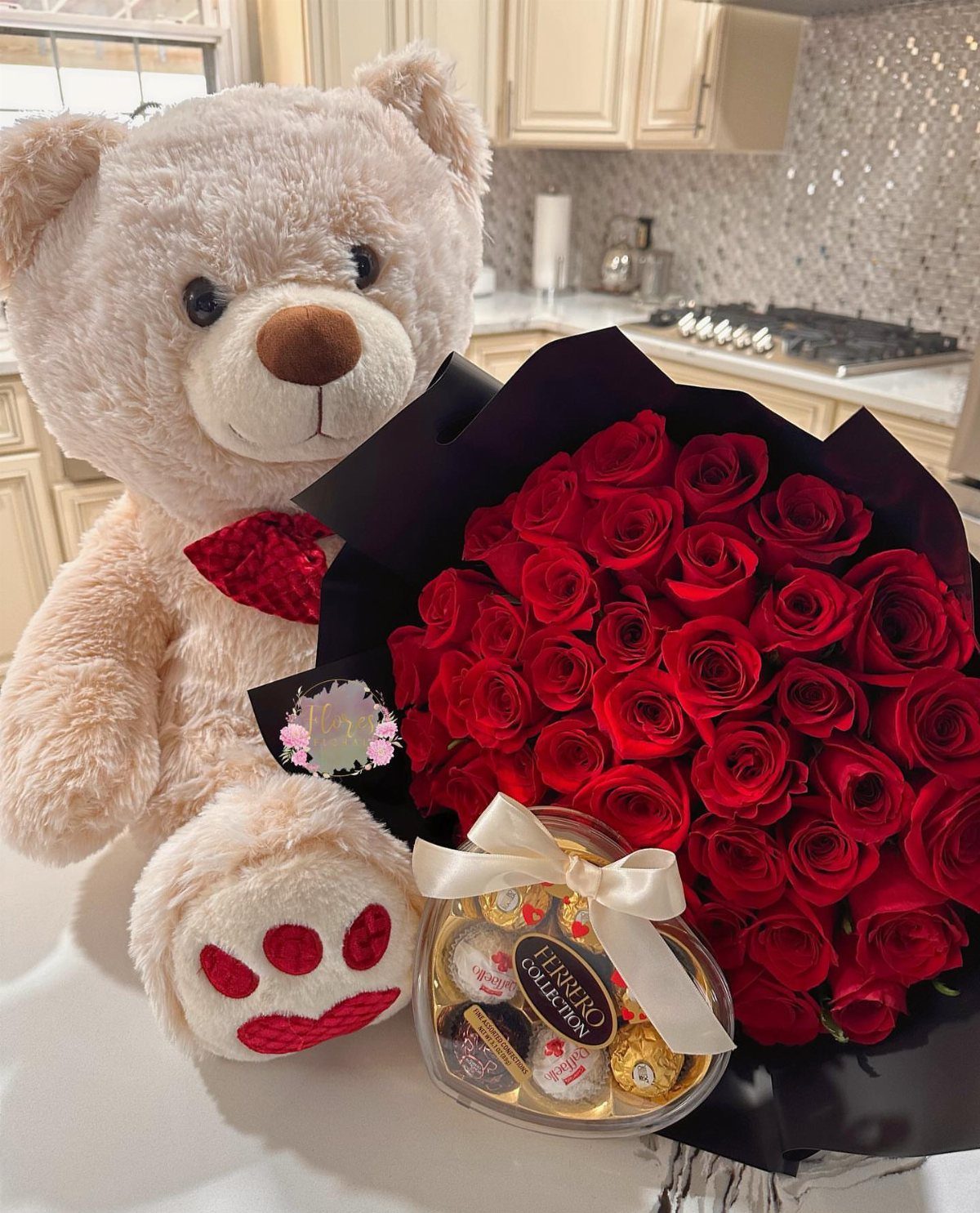 Beige teddy bear, red rose bouquet, and heart-shaped chocolate box on white table.