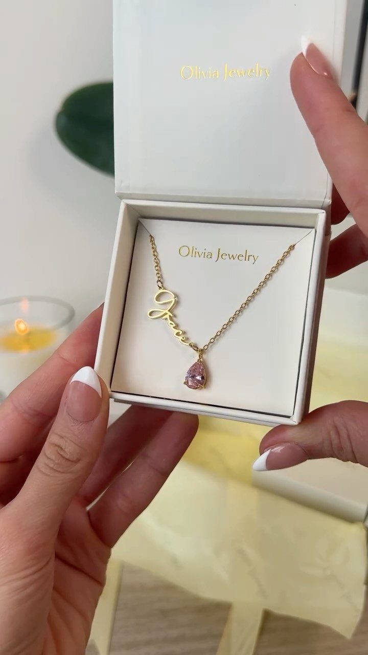 Gold necklace with a script L and pink gemstone in a white box