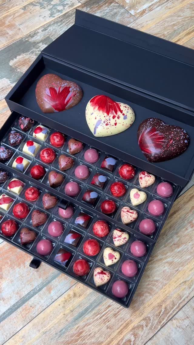 Assorted heart-shaped gourmet chocolates in a black gift box on a wooden table