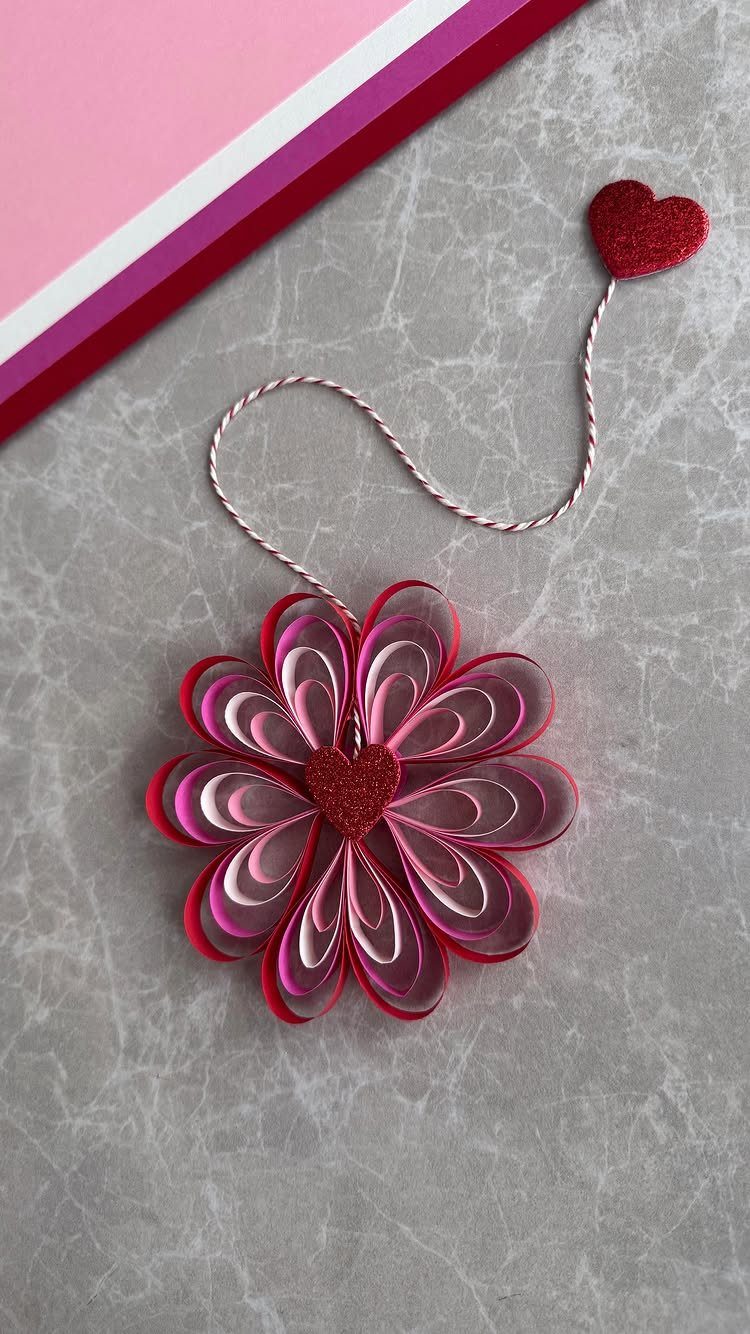 Quilled paper flower with red heart center and a small heart on a wire.