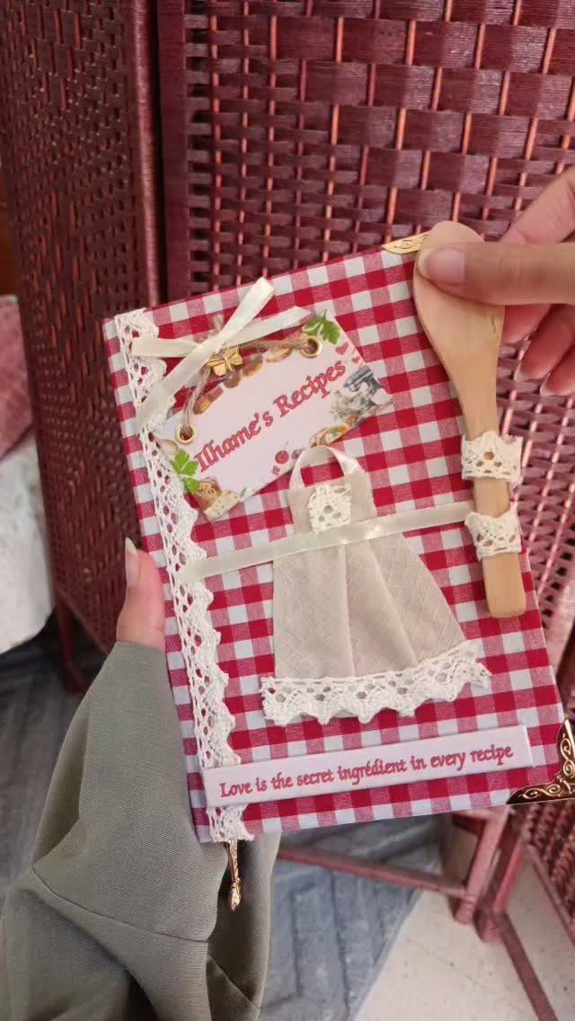 Handmade recipe book with red checkered cover, fabric apron, and wooden spoon.