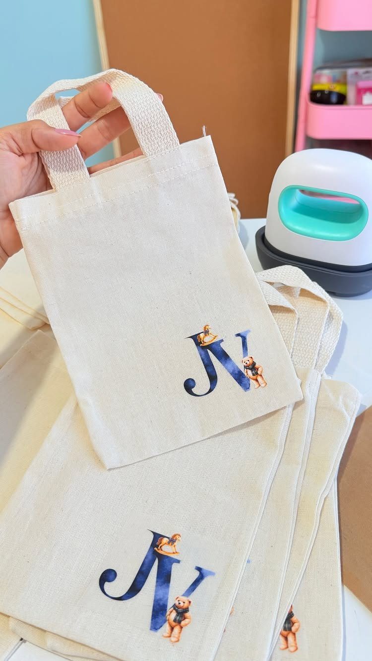 Cream canvas tote bags featuring a blue monogram letter N with teddy bears.