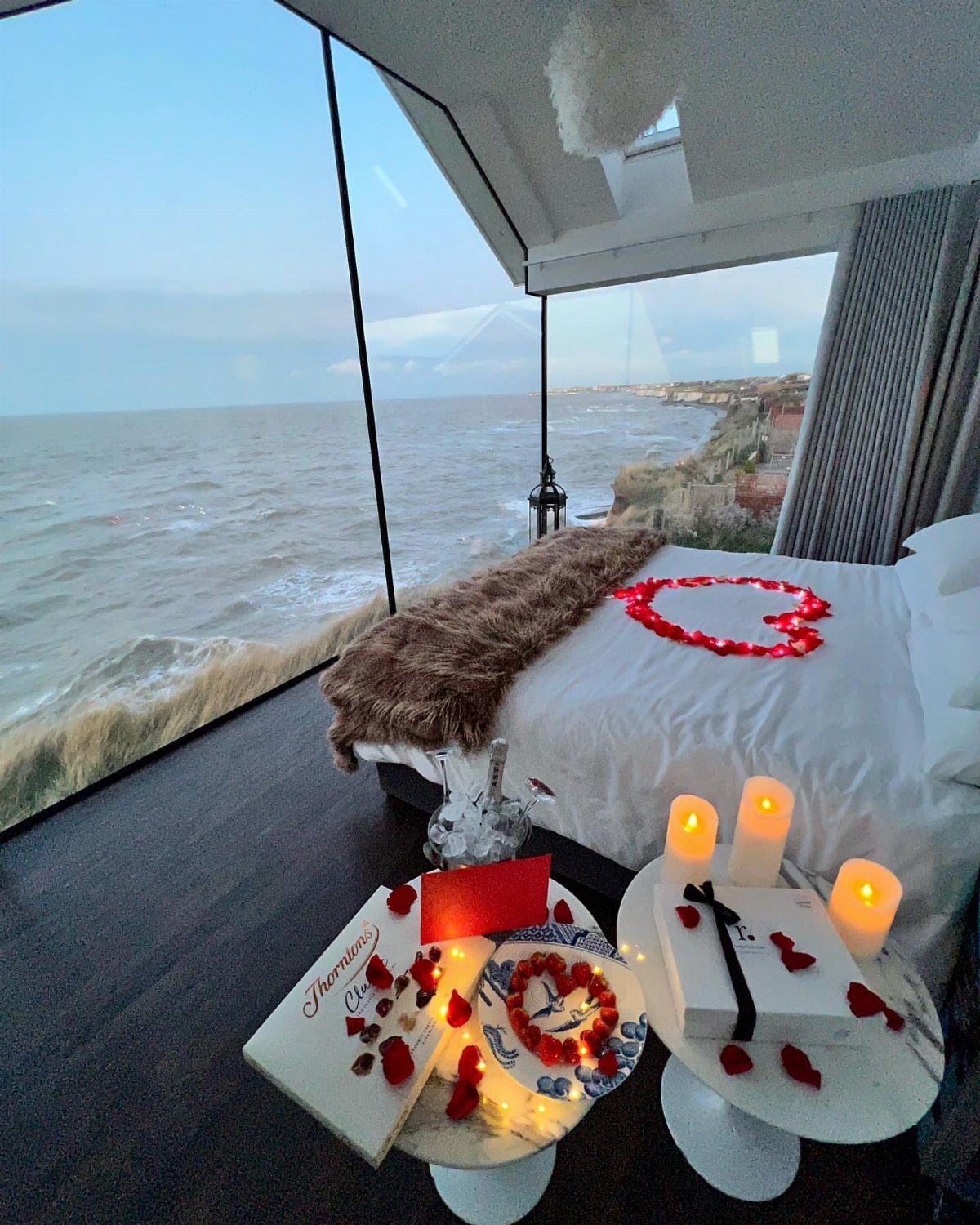 Romantic hotel room with rose petal heart on bed overlooking a coastal cliff