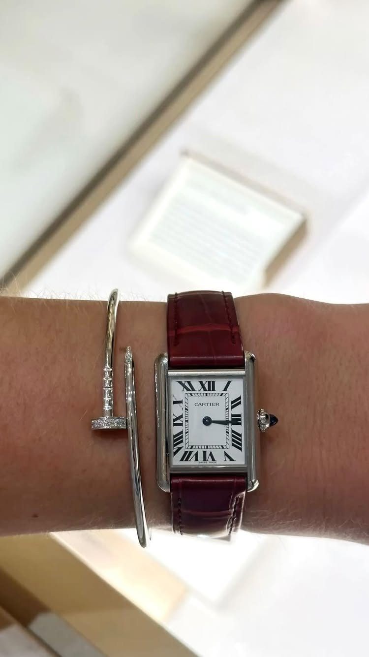 Rectangular silver watch with red leather strap and silver bracelets on a wrist.