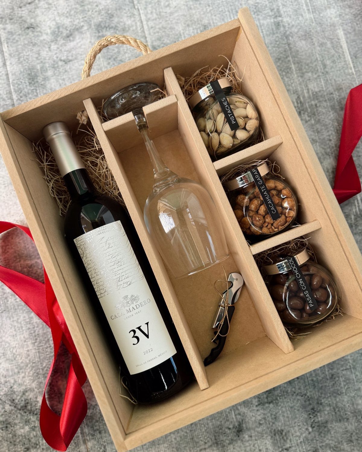 Wooden gift box with red wine, a wine glass, and gourmet snack jars.