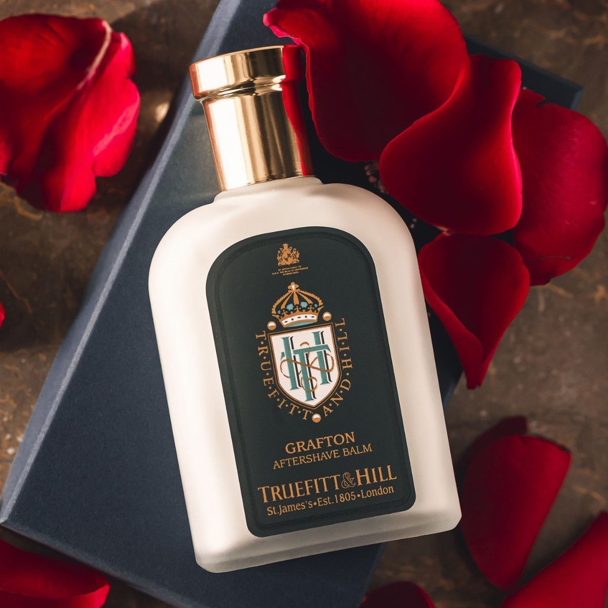 Aftershave balm bottle on a blue box surrounded by red rose petals.