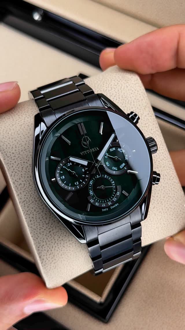 Black analog wristwatch with a dark green face held in a presentation box.