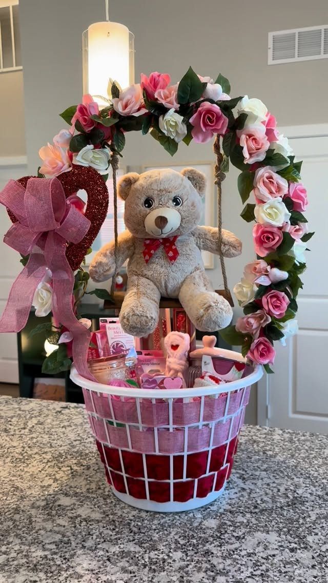 Valentine gift basket with a teddy bear on a swing and floral arch.