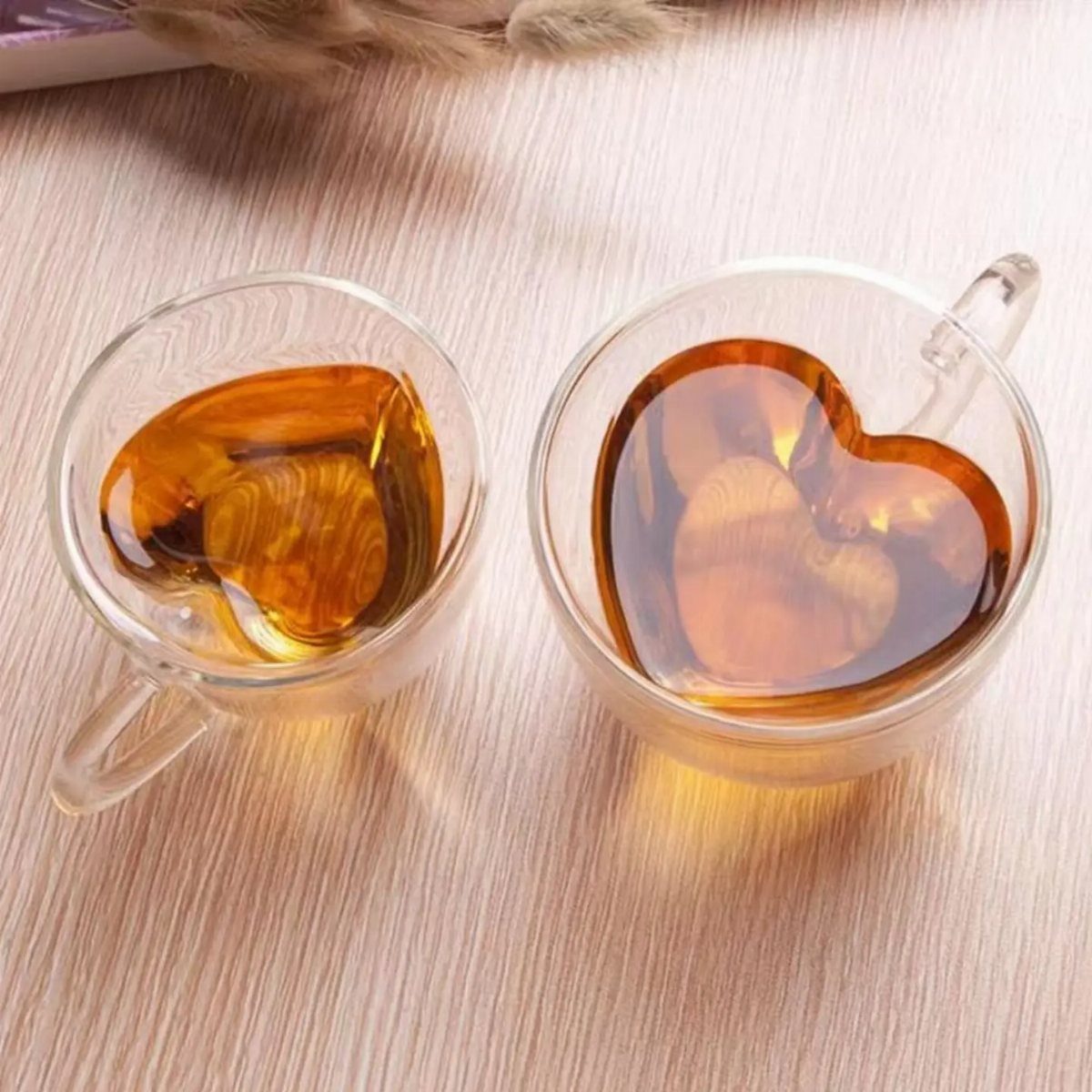 Two clear glass mugs with heart-shaped bottoms filled with amber tea on wood.