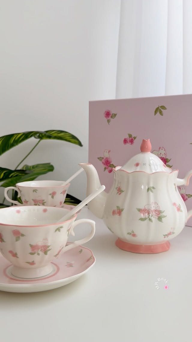 Floral ceramic teapot and teacups with a pink card on a white table