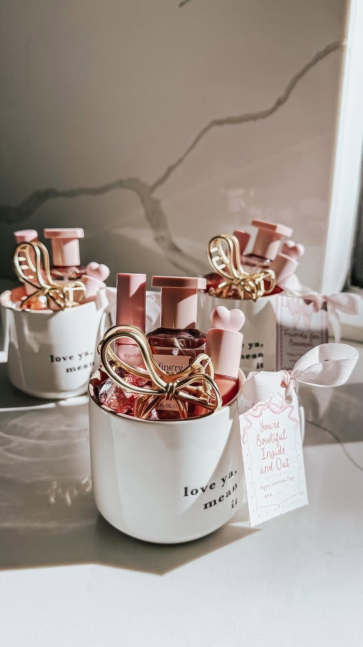 White mugs filled with pink beauty products and gold knots as Valentine's gifts.