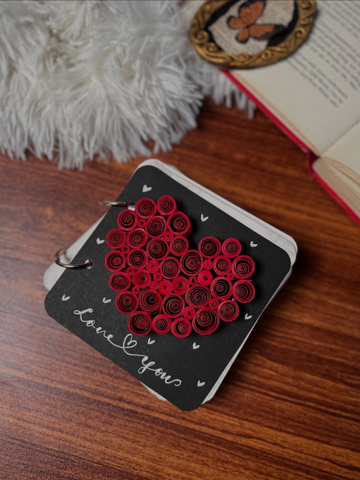 Black notebook with a red quilled paper heart and Love you text.