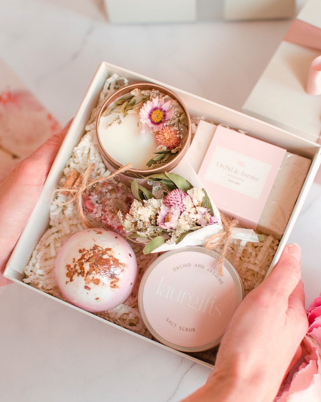 Spa gift box containing a bath bomb, salt scrub, candle, and pink soap.