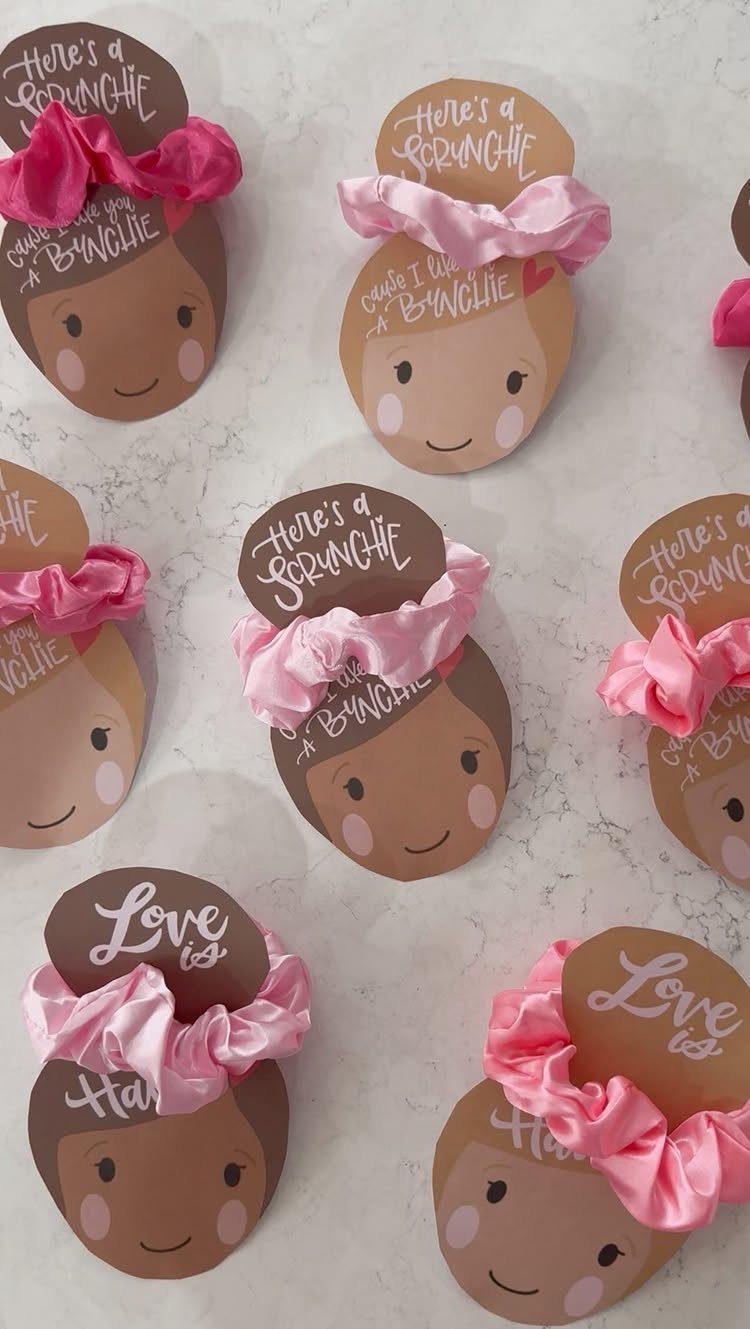 Printed cardstock face cutouts with pink scrunchies attached as Valentine's Day gifts.