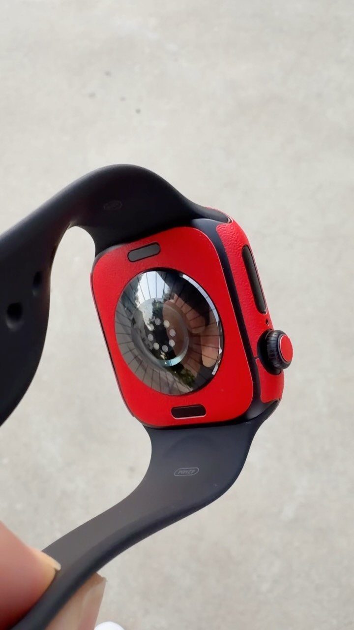 Apple Watch with a red protective case and black strap held by hand.