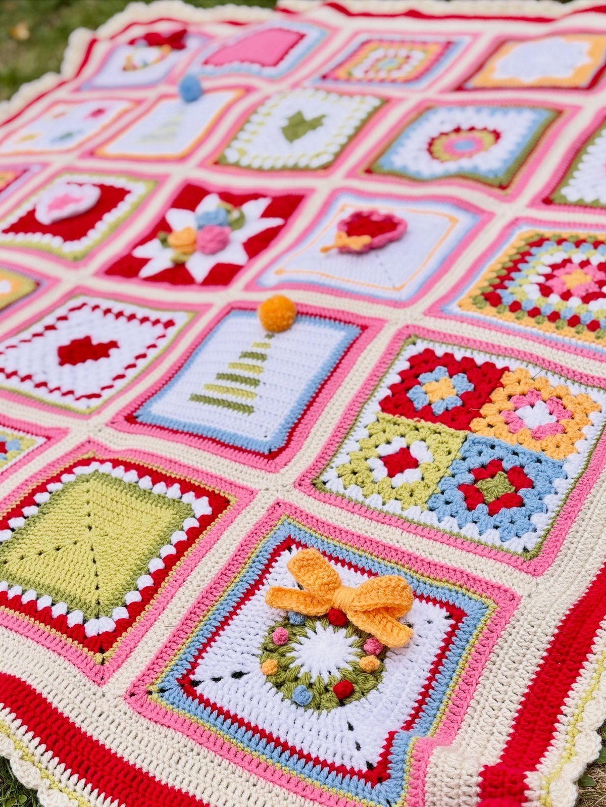 Colorful crochet blanket with holiday patterns spread across a green grass lawn.