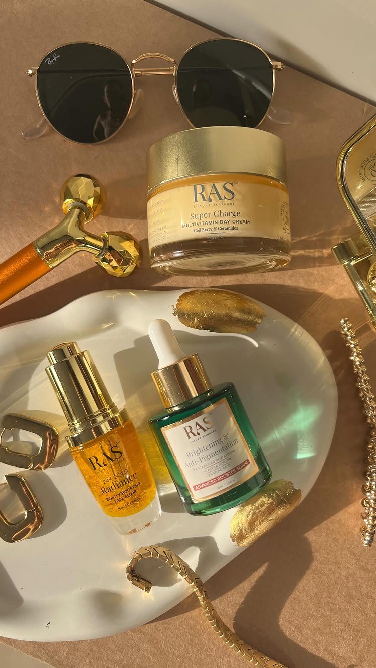 RAS skincare products with gold accents, sunglasses, and jewelry on a white tray.