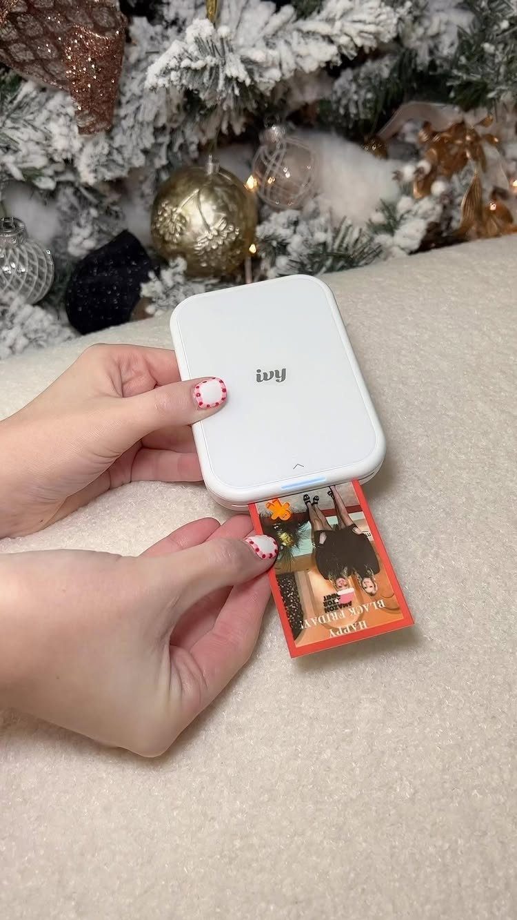 White portable photo printer printing a small photo near a decorated Christmas tree.