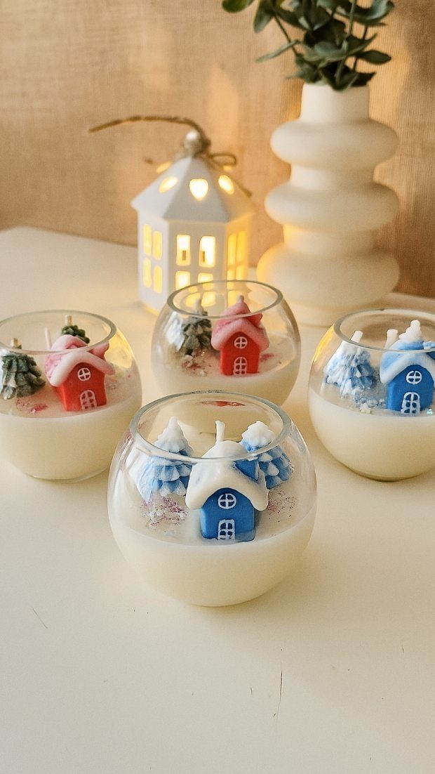 Four glass bowl candles with miniature colorful houses and trees in white wax.