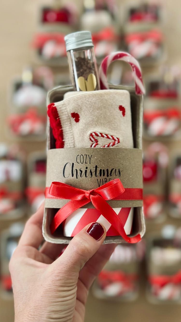 Hand holding a Christmas gift box with socks, candy cane, and red ribbon.
