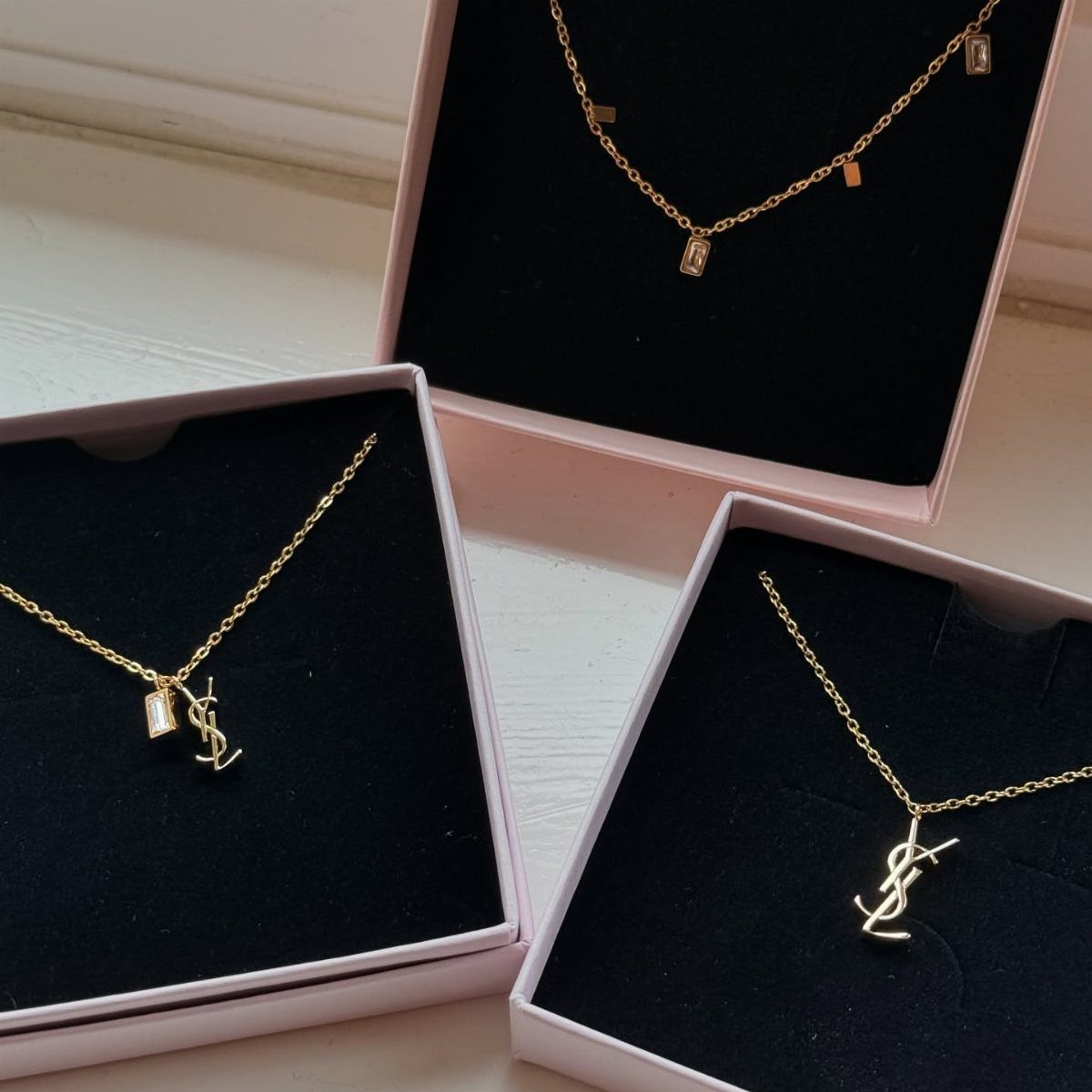 Three gold necklaces in pink jewelry boxes, including two with YSL logo pendants.