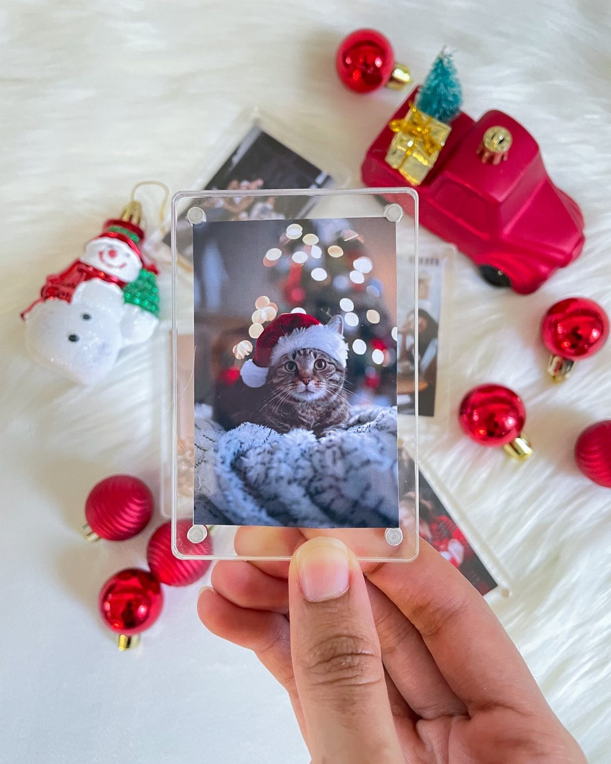 Hand holding a framed photo of a cat in a Santa hat among ornaments