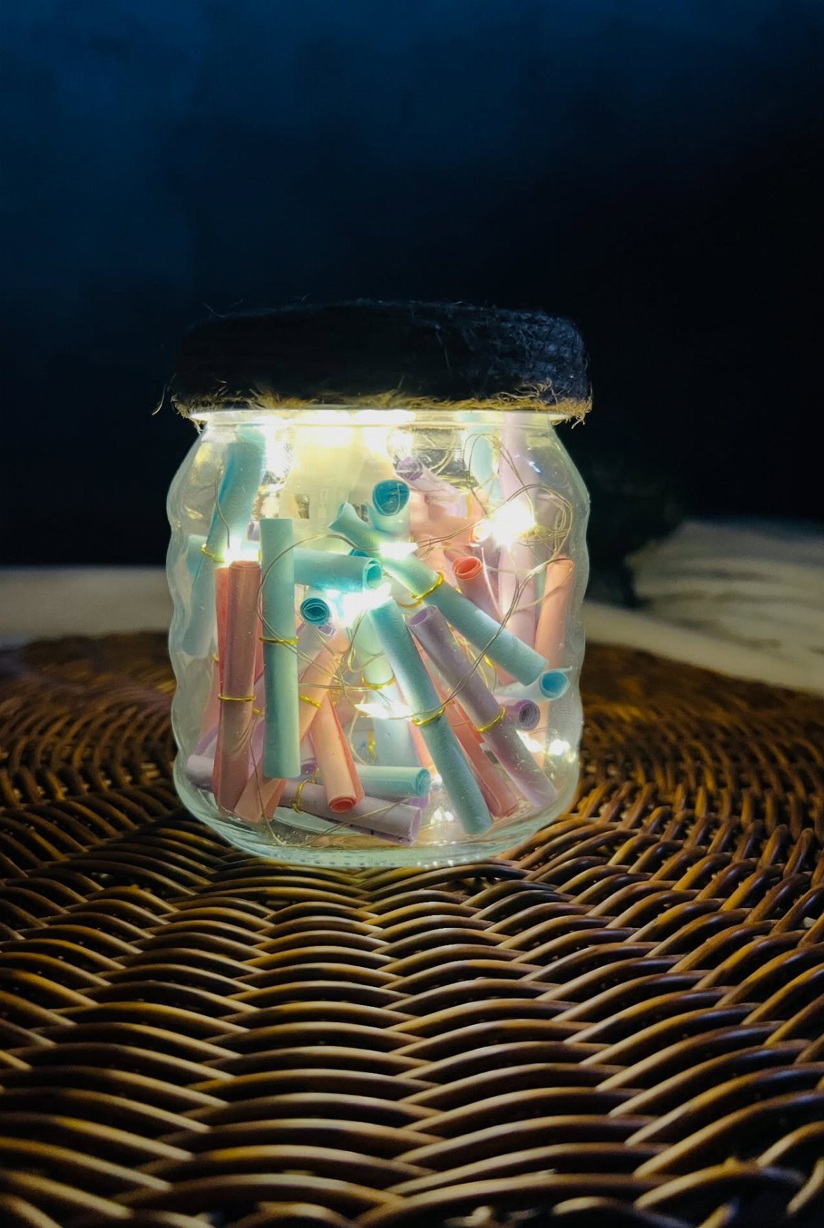 Glass jar filled with colorful rolled paper notes and glowing fairy lights