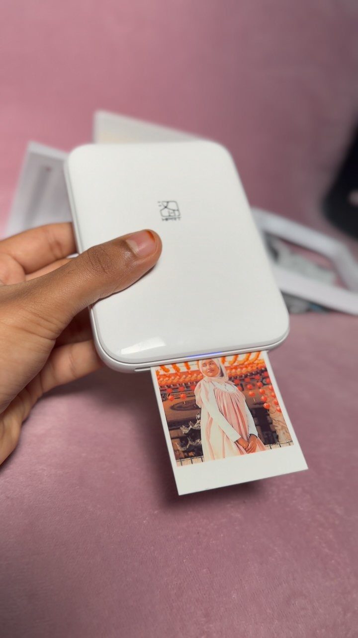 Small white portable photo printer printing a square instant photo of a woman.