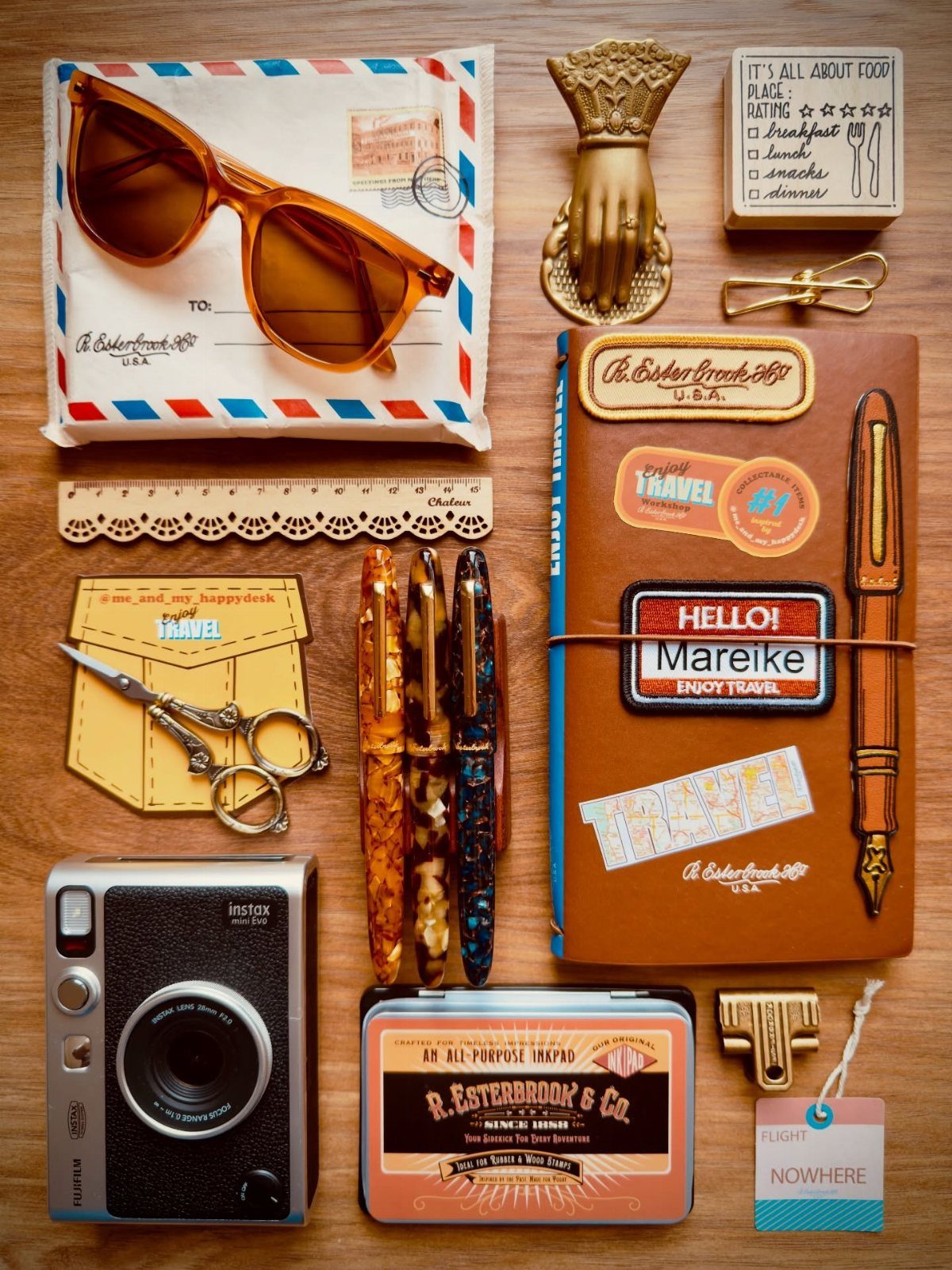 Brown leather travel journal surrounded by vintage camera, sunglasses, and stationery on wood.