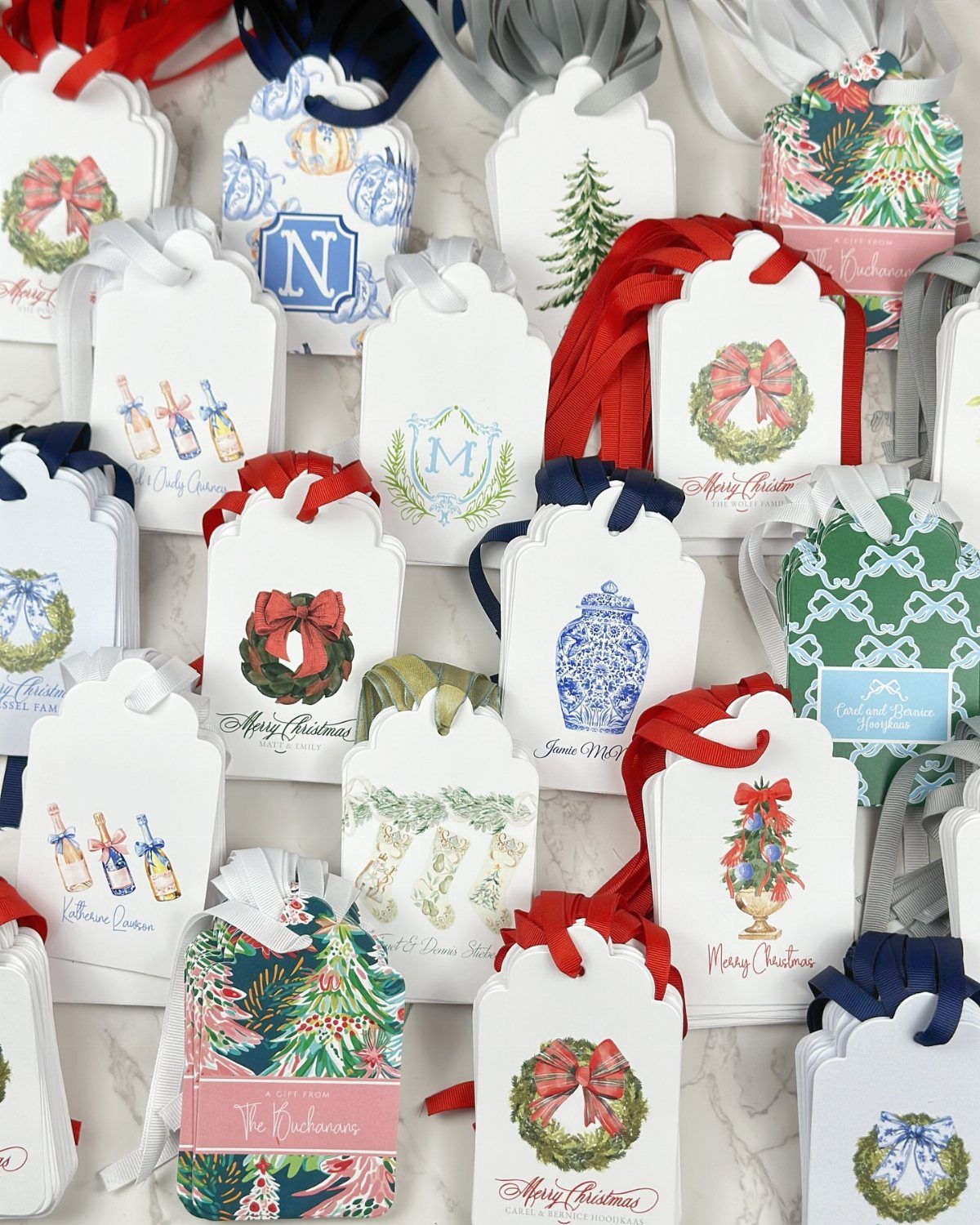 Holiday gift tags with wreaths and ribbons scattered on a white marble surface