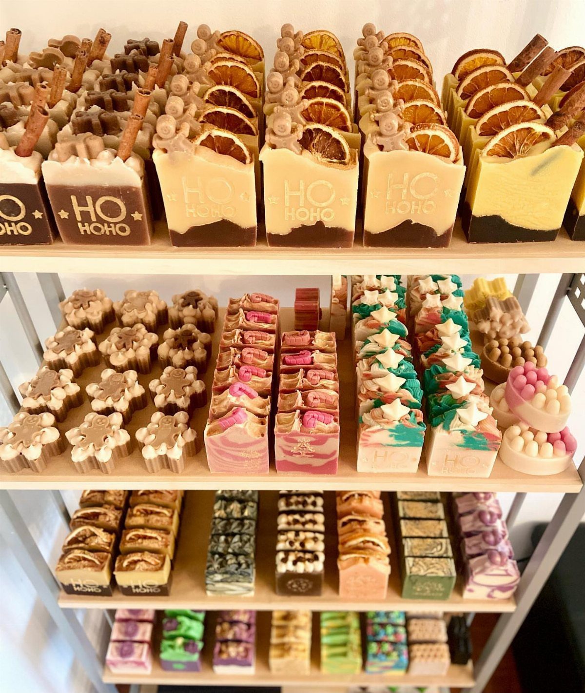 Handmade holiday soaps with orange slices and festive patterns on white shelves