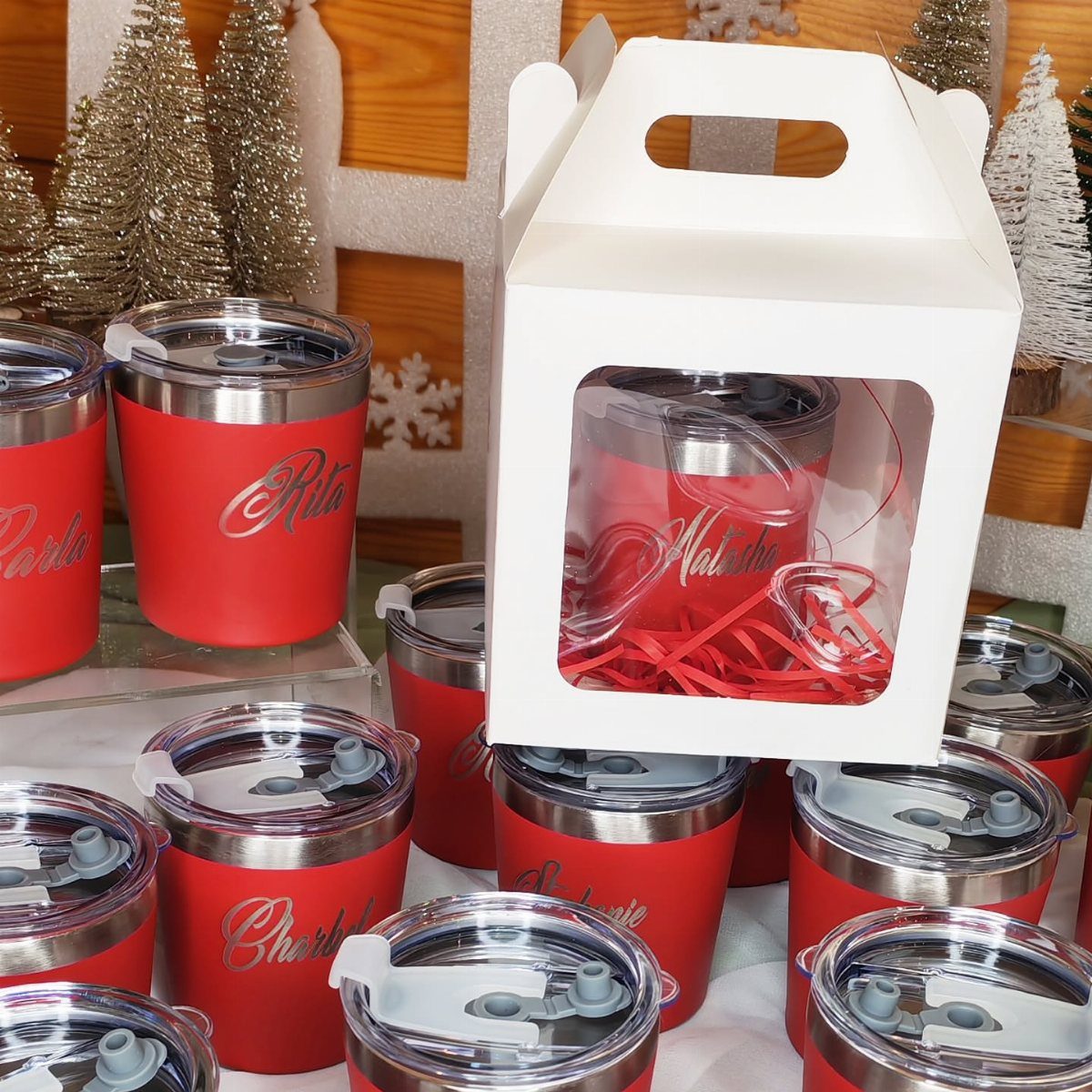 Red personalized travel mugs with names, one in a white gift box.